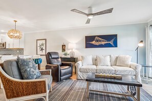 Ein modernes Wohnzimmer mit einem schwarzen Ledersessel, einem weißen Sofa, einem Essbereich mit weißem Tisch und einem Deckenventilator.