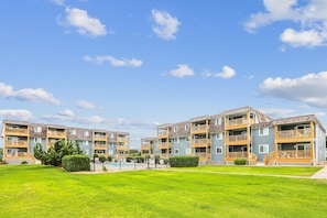 Un immeuble résidentiel à plusieurs étages, doté de balcons, d’une piscine et d’une pelouse bien entretenue.