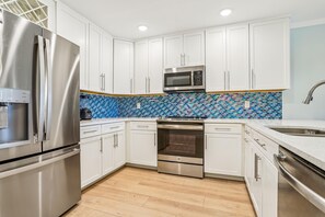 A modern kitchen with stainless steel appliances, white cabinetry, and a blue-tiled backsplash.