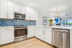 A modern kitchen with white cabinets, a stainless steel dishwasher, and a colorful backsplash. - New Listing -- 3 BR Oceanfront Condo in Duck with pool (Duck)