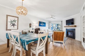 A dining area with a table set for four, a ceiling fan, and a television mounted on the wall.
