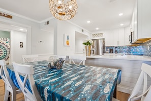 Une cuisine moderne avec des meubles blancs, une nappe à motifs bleus et un tableau décoratif représentant un ananas.