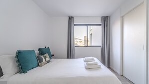 A modern hotel room with a large bed, grey curtains, and a view of buildings through the window.