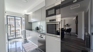 A modern kitchen with stainless steel appliances, a glass door leading to a balcony, and a dining area with a black table and chairs.