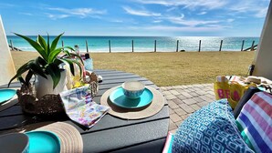 Une terrasse avec vue sur la plage, une table avec un saladier, une plante et un sac.