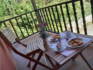 A wooden table with a white tablecloth, two plates of cookies, a cup, and a small potted plant on a balcony with a railing. - Vivienda Vacacional LA Carlota (Llanes- Asturias)