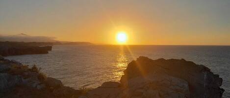 A sunset over a coastal landscape with rocky outcrops and calm sea.