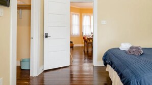 Una habitación de hotel con una cama, una puerta que da a un comedor y un cubo azul.