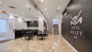 Moderni hotellin aula, jossa on marmorilattia, ruokailutila tuoleineen ja pöytineen sekä portaikko, joka johtaa toiselle tasolle.