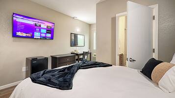 A hotel room with a bed, a desk, a chair, a TV mounted on the wall, and a door.