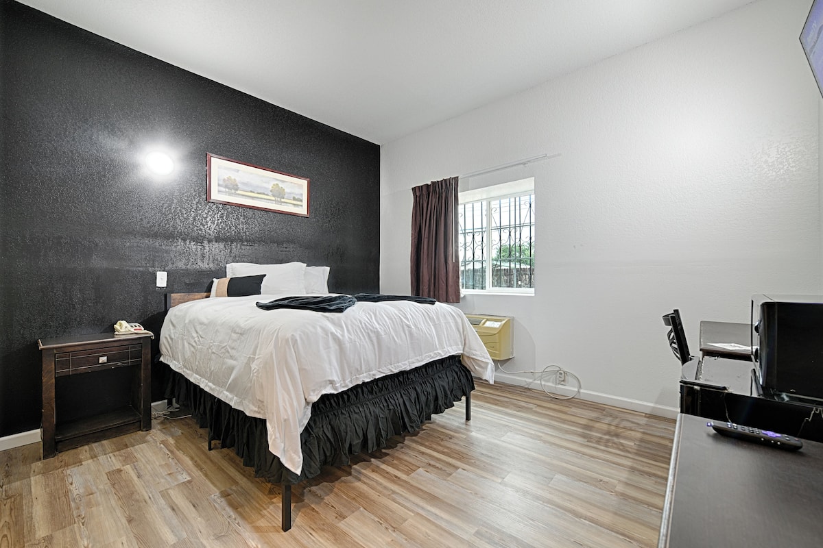 A bedroom with a bed, a bedside table, a TV, and a window with curtains.