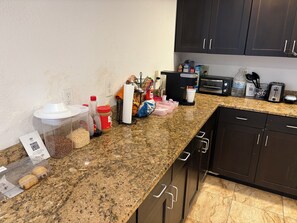 A kitchen with granite countertops, a coffee maker, a toaster, and various kitchen items. - Hotel Dilley Grand (Dilley)