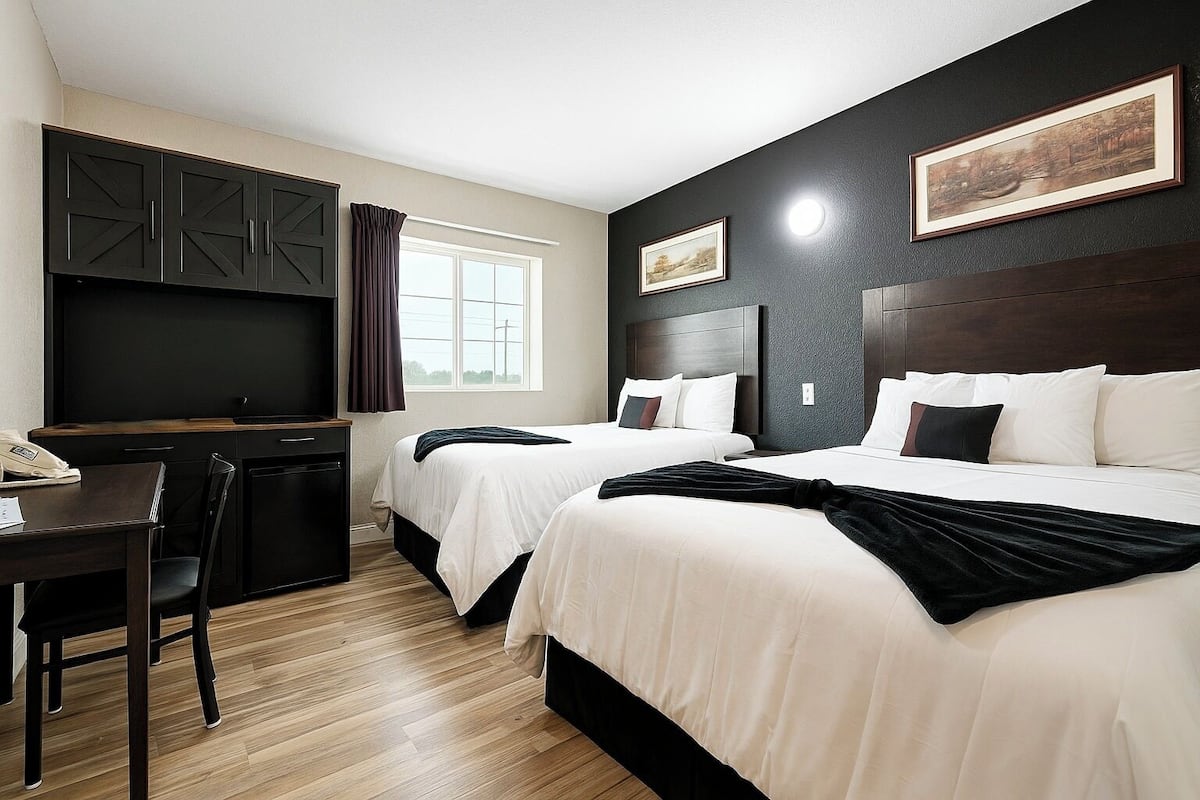 A hotel room with two beds, a desk, a chair, and a TV.