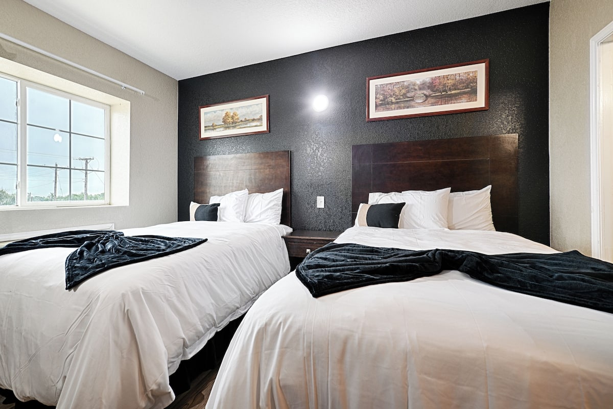 A hotel room with two beds, a large window, and artwork on the walls.