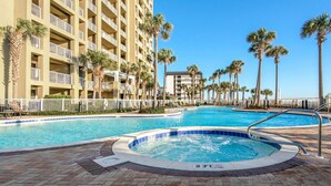 A hotel pool area with a hot tub, palm trees, and a multi-story building in the background. - PET FRIENDLY! PENTHOUSE! 4/3 SLEEPS 11! BCH SRVC INCL!!! (Panama City Beach)