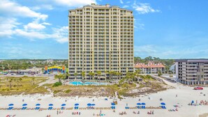 A tall hotel with multiple balconies, a pool area, and a beach with sun loungers. - PET FRIENDLY! PENTHOUSE! 4/3 SLEEPS 11! BCH SRVC INCL!!! (Panama City Beach)