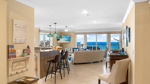 A spacious living area with a kitchen, bar, and large windows offering a view of the ocean. - PET FRIENDLY! PENTHOUSE! 4/3 SLEEPS 11! BCH SRVC INCL!!! (Panama City Beach)