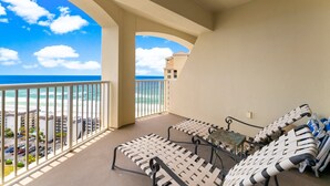 A balcony with two lounge chairs, a small table, and a view of the ocean and buildings. - PET FRIENDLY! PENTHOUSE! 4/3 SLEEPS 11! BCH SRVC INCL!!! (Panama City Beach)