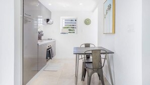 A compact kitchen with modern appliances, a dining table with chairs, and a framed picture on the wall. - Renovated Apartment with pool at the garden #6 (Pelican Key)