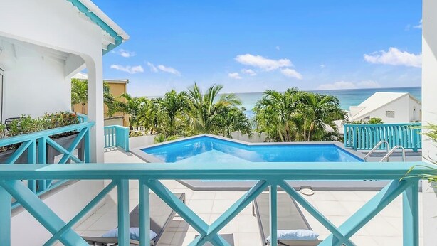 A pool area with a view of the ocean, surrounded by palm trees and a white building. - Renovated Apartment with pool at the garden #6 (Pelican Key)