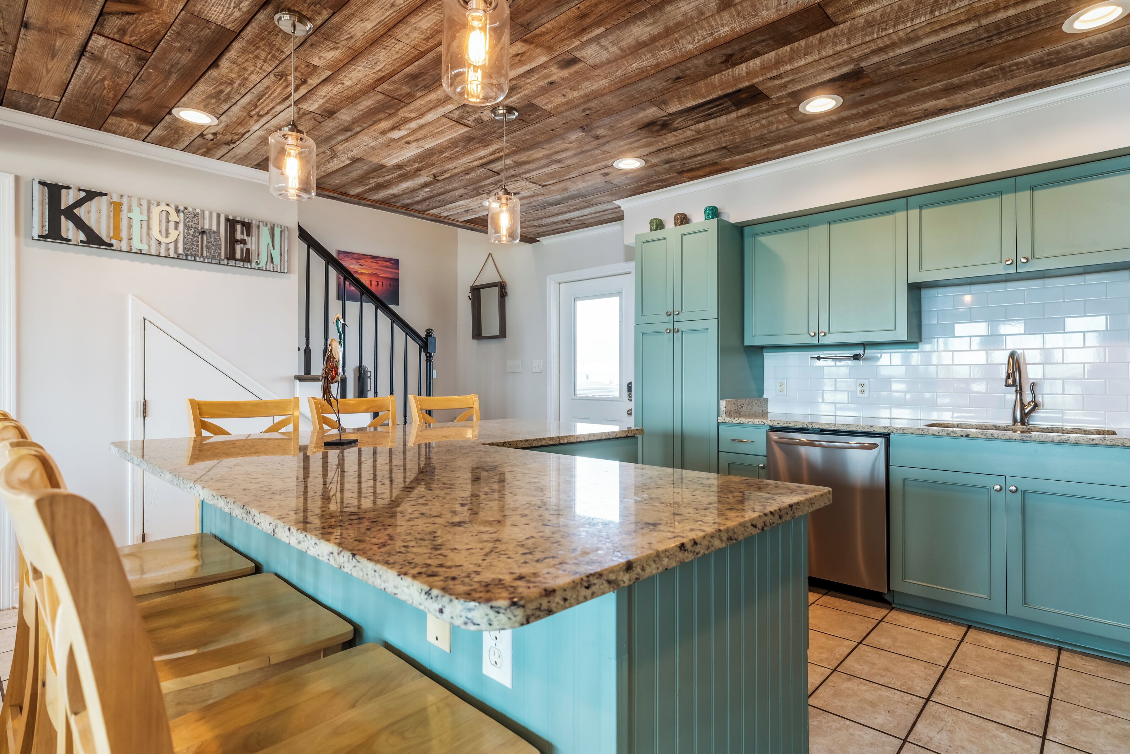 Une cuisine avec des armoires de couleur turquoise, un îlot en granit, des chaises en bois et un plafond en bois.