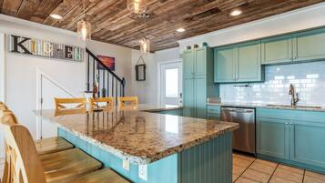 Une cuisine avec des armoires de couleur turquoise, un îlot en granit, des chaises en bois et un plafond en bois.