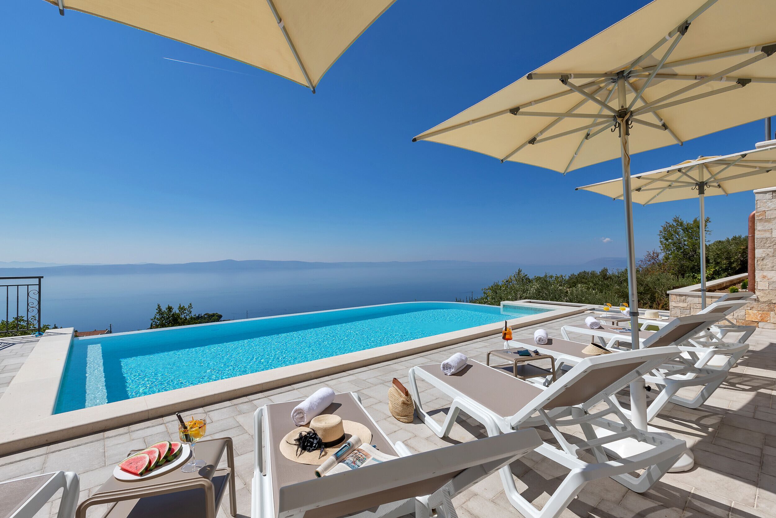 A poolside area with lounge chairs, umbrellas, and a view of the sea.