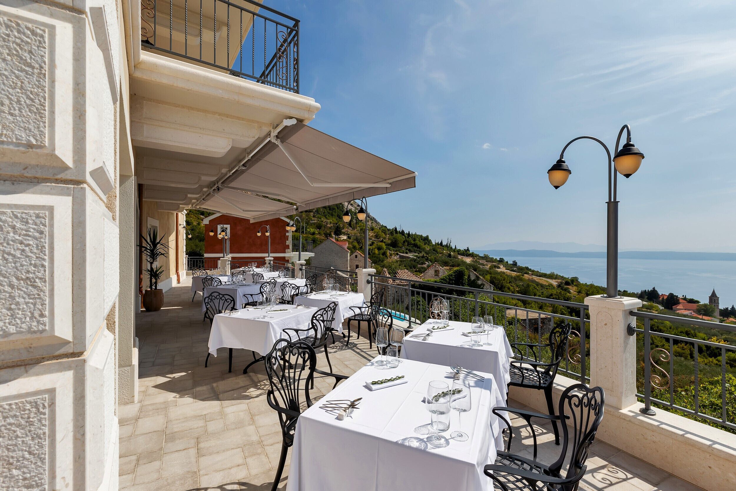 Un espace de restauration en plein air avec des tables et des chaises, un coin salon abrité et une vue sur la mer.