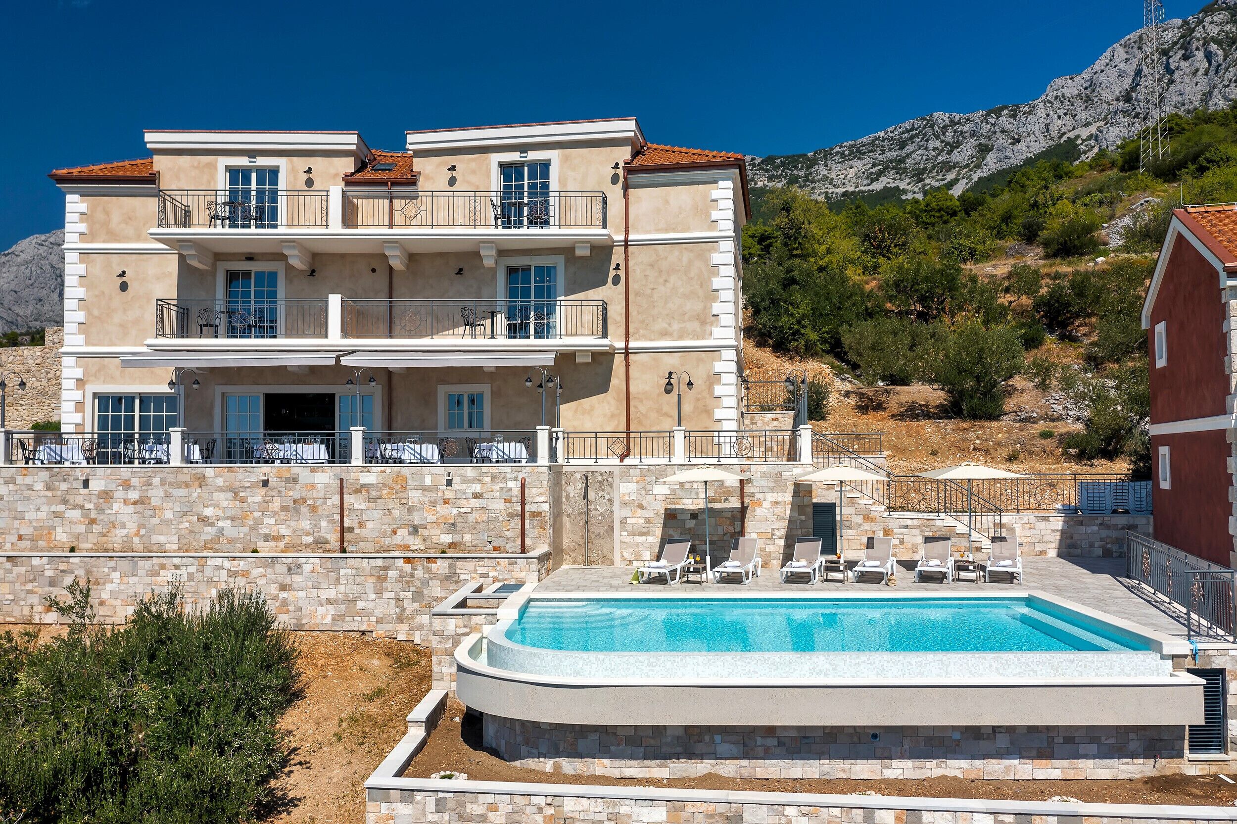 Un edificio a più piani con piscina, area salotto esterna e montagne sullo sfondo.