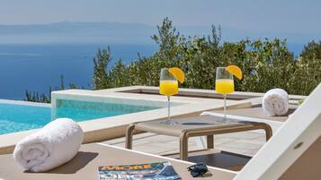 A poolside lounge with two glasses of orange juice, a rolled towel, and a magazine on a table.