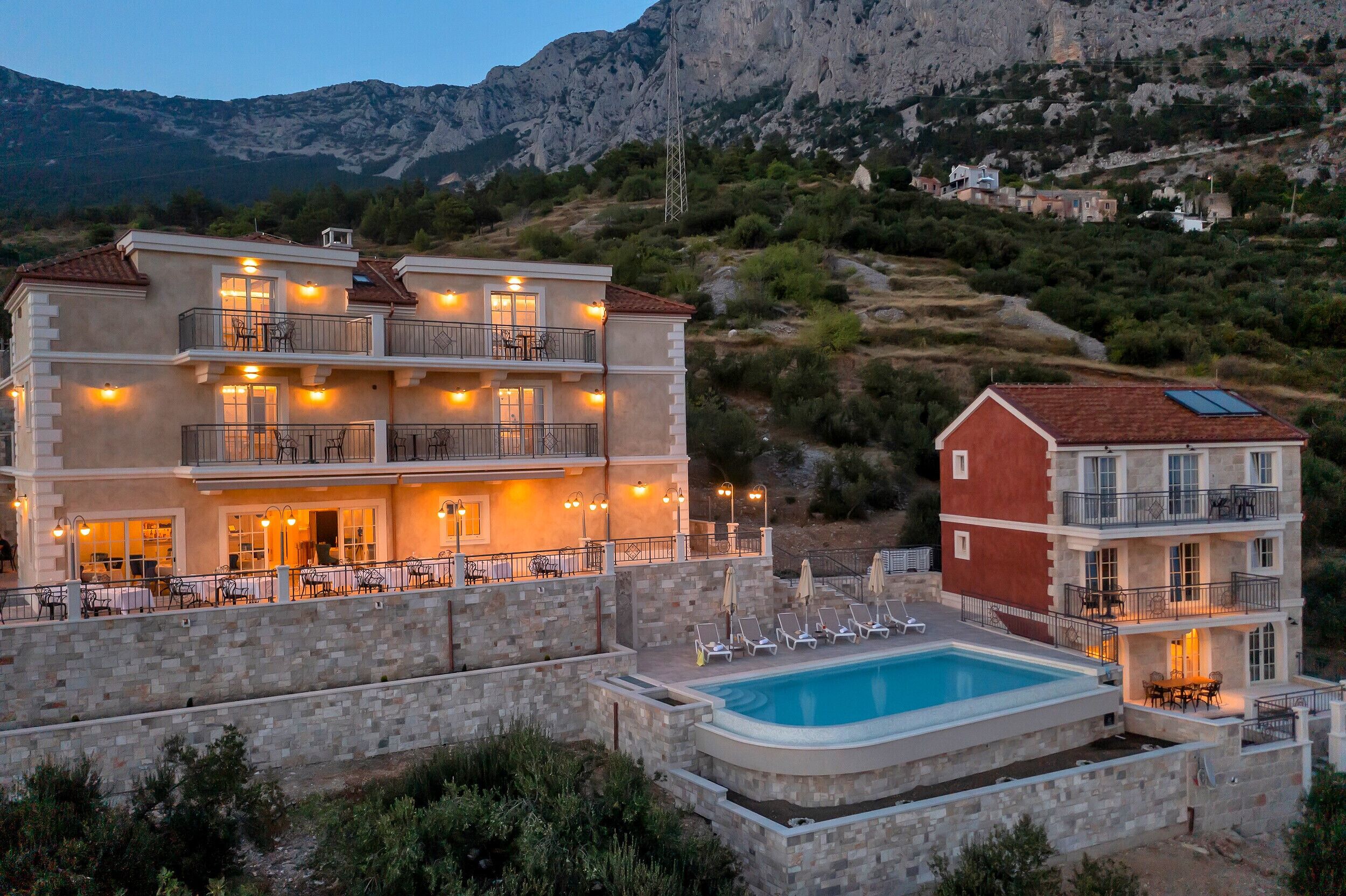 Un edificio a più piani con piscina, area salotto esterna e vista su un paesaggio montuoso.