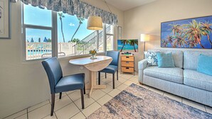 A living room with a sofa, two chairs, a small table, a lamp, and a painting of palm trees.