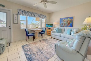 Un salon comprenant un canapé, une table à manger avec des chaises, un téléviseur et un ventilateur de plafond.