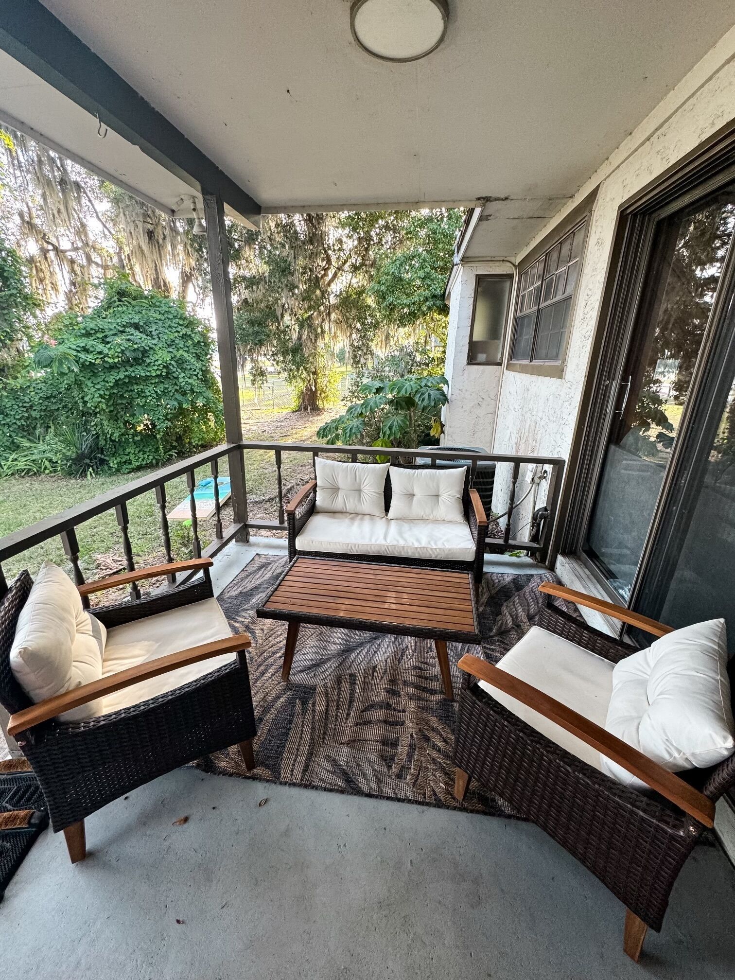 A covered patio with wicker furniture, a wooden table, and a view of the garden.