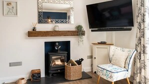 A living room with a fireplace, a television mounted on the wall, a chair, and a wooden shelf with decorative items. - Cute & Cosy Cottage | Chilterns - Pass the Keys (Princes Risborough)