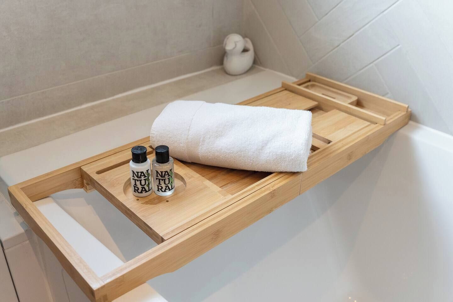 Ein Holztablett mit einem weißen Handtuch und zwei Flaschen auf einer Badezimmerablage.
