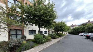 Une rue résidentielle bordée d’arbres, avec des voitures garées, une rangée de maisons et un trottoir.