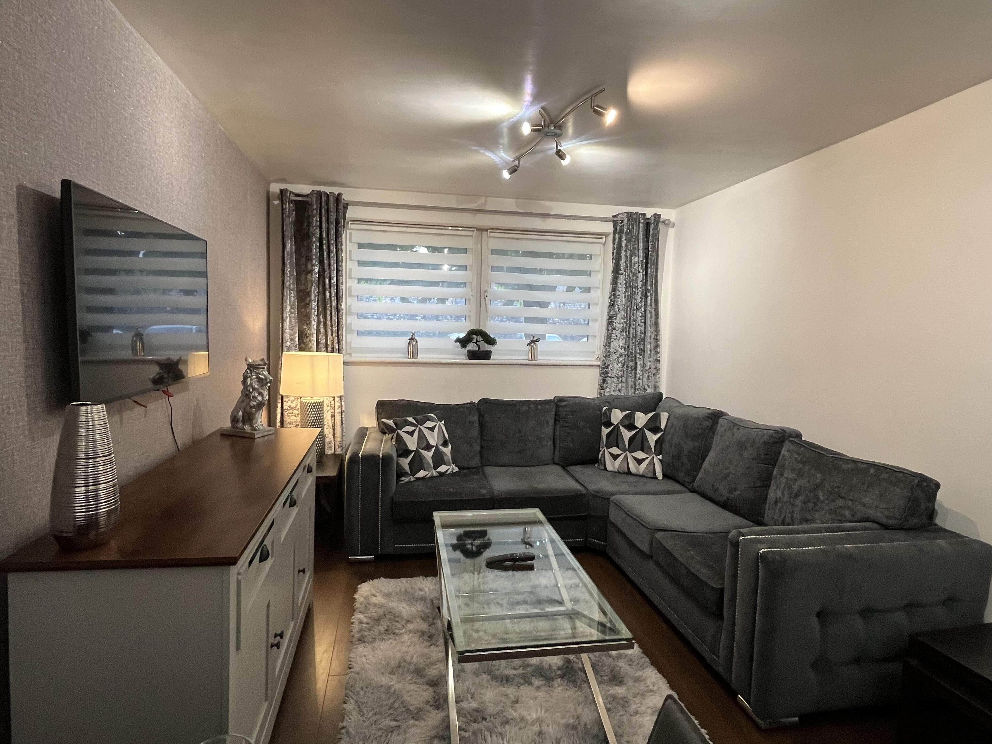 A modern living room with a sofa, a coffee table, a TV, and a window with curtains.