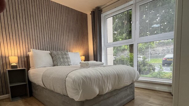 Une chambre à coucher moderne avec un grand lit, une table de chevet, une lampe et une fenêtre avec des stores.