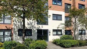 Un immeuble d’appartements moderne, doté d’une façade plane, de nombreuses fenêtres et d’un petit espace d’entrée avec une porte et une boîte aux lettres.
