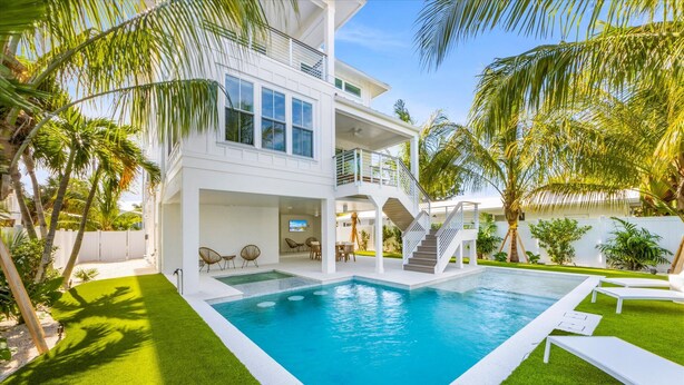 A modern two-story house with a swimming pool, outdoor seating, and palm trees. - AMI Escape! Swim-Up Bar, Ping Pong, Spa and Walk to Beach (Anna Maria)