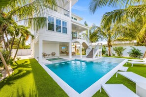 A modern two-story house with a swimming pool, outdoor seating, and palm trees.