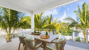 A covered outdoor dining area with wicker chairs and a table set for two, overlooking a tropical landscape with palm trees. - AMI Escape! Swim-Up Bar, Ping Pong, Spa and Walk to Beach (Anna Maria)