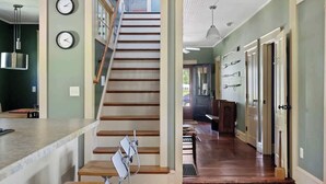 Una escalera que lleva al segundo piso, una zona de cocina con mostrador y un pasillo con puertas y una lámpara colgante.