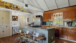 Una cocina con armarios de madera, una isla central con taburetes, un refrigerador y una ventana.