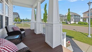 Eine überdachte Veranda mit Korbmöbeln, Blick auf eine Wohnstraße und einen klaren Himmel.