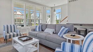 Ein Wohnzimmer mit grauem Sofa, gestreiftem Ohrensessel, Couchtisch und kleinem runden Tisch mit Fernbedienung.
