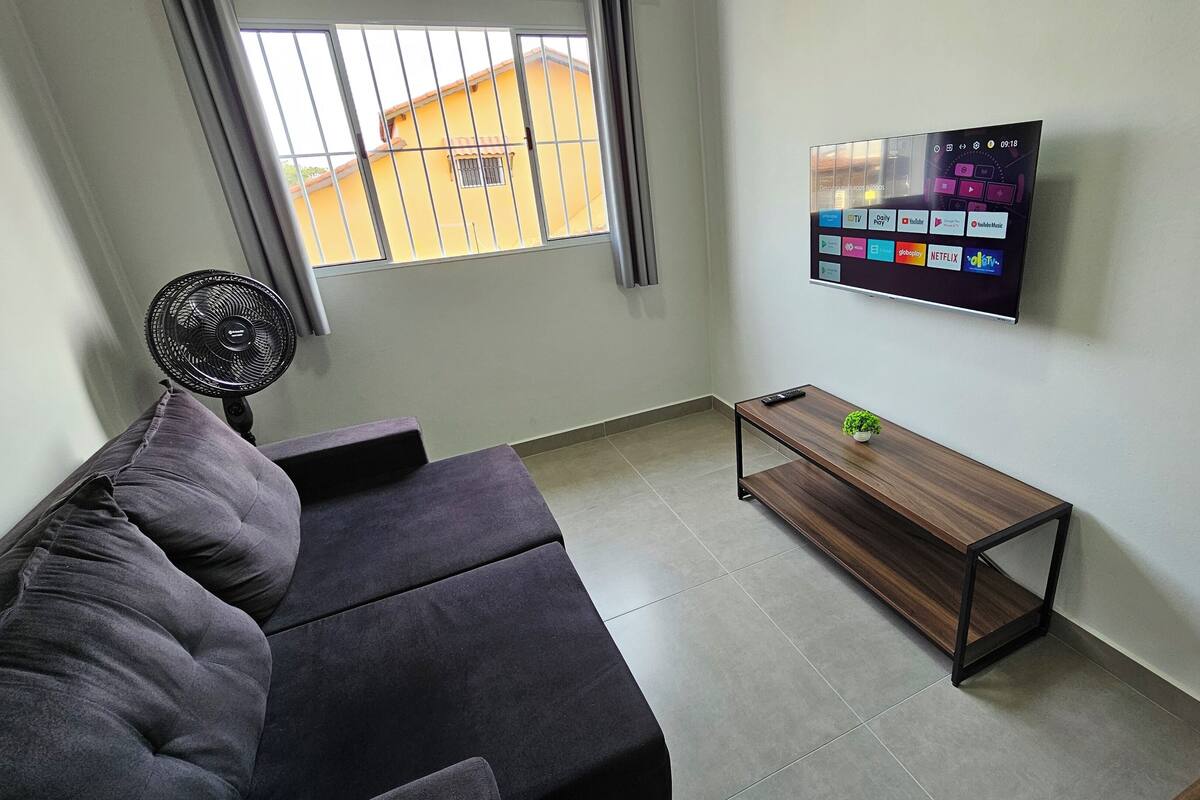 A modern living room with a grey sofa, a wooden coffee table, and a TV mounted on the wall displaying streaming services.