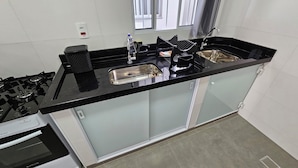 Una cocina moderna con encimera negra, pileta de acero inoxidable y cocina a gas.