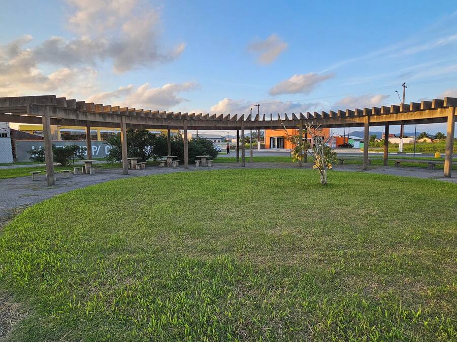 A covered outdoor area with a pergola structure, seating, and a grassy lawn.